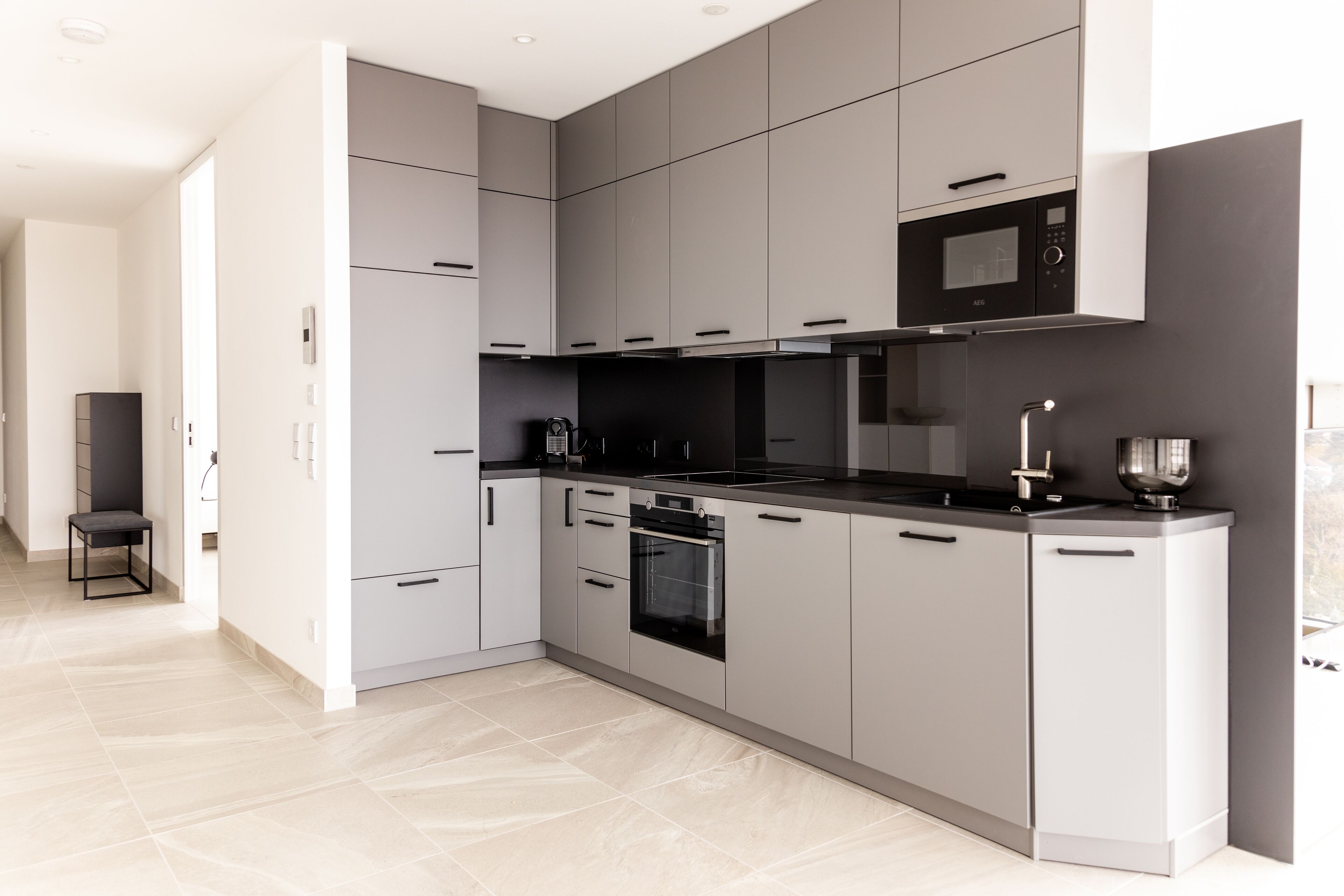 A modern kitchen with grey cabinetry, a black countertop, and a built-in oven.