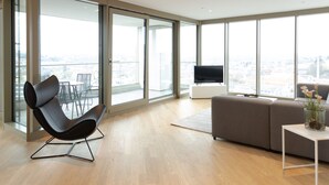Una sala de estar moderna con un ventanal grande, un sillón de cuero negro, un sofá gris y una mesita con un jarrón de flores.