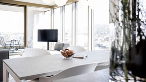 Un comedor moderno con una mesa grande, sillas blancas, un tazón de bocadillos y vistas de la ciudad a través de amplios ventanales.