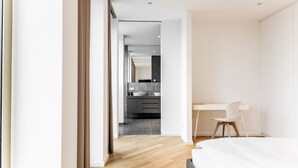 Una habitación de hotel moderna con suelo de madera, cama, escritorio y vistas al baño.