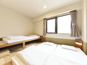Habitación de hotel con dos camas individuales, una ventana con cortinas, una mesita de noche con lámpara y suelo de madera.