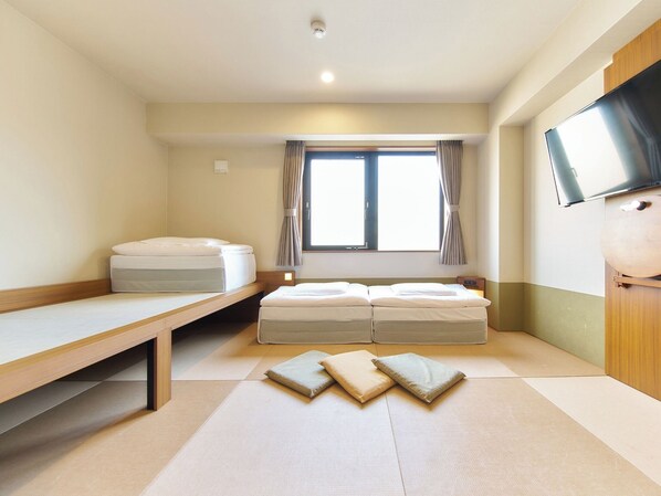 Una habitación con cama, escritorio, televisión y ventana con cortinas.