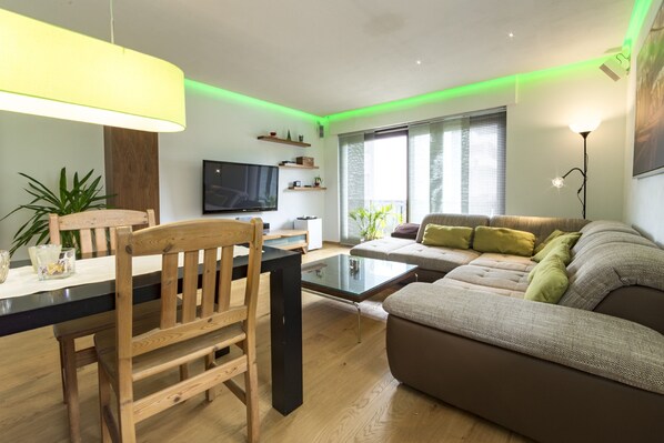 A modern living room with a wooden dining table, a sofa, and a flat-screen TV. - Ferienwohnung Whiskey (Winterberg)