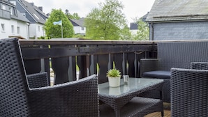 An outdoor patio area with wicker furniture, a glass table, and a wooden deck. - Ferienwohnung Whiskey (Winterberg)