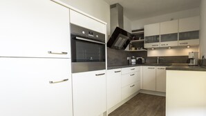 A modern kitchen with white cabinets, a built-in oven, and a coffee machine. - Ferienwohnung Whiskey (Winterberg)