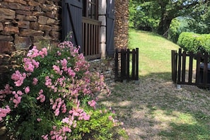 A stone building with a wooden gate, a paved path, and pink flowering bushes.