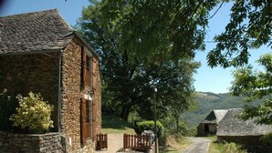 A stone building with a gravel driveway and wooden gates, surrounded by trees and hills. - Converted Stone Barn with Pool (Occitanie)