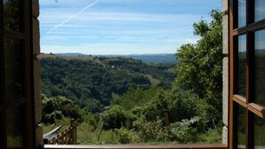 A view through a window of a lush, green landscape with rolling hills and a clear sky. - Converted Stone Barn with Pool (Occitanie)