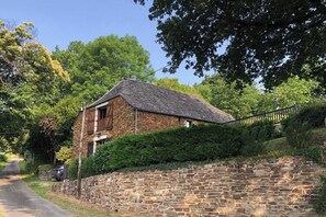 A stone house with a thatched roof, surrounded by greenery and a stone wall.