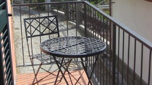 Un balcón con una mesa redonda de metal y dos sillas, con vistas a una zona costera con colinas y una masa de agua.