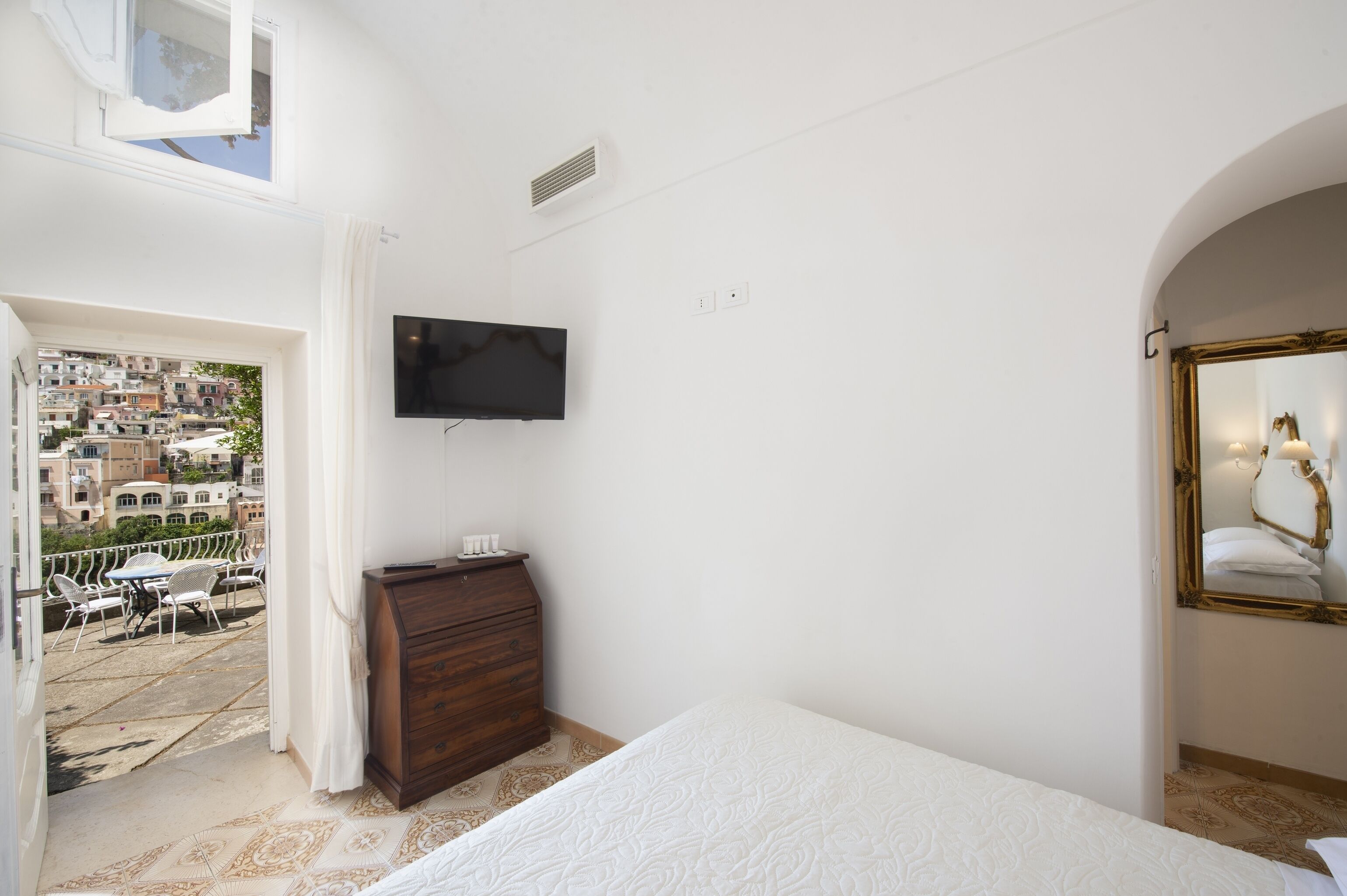 Een slaapkamer met een bed, een dressoir, een televisie en een balkon met uitzicht over de stad.