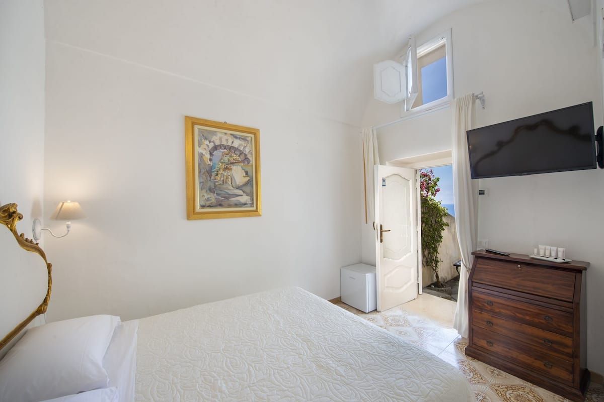 A bedroom with a bed, a dresser, a television, and a painting on the wall.