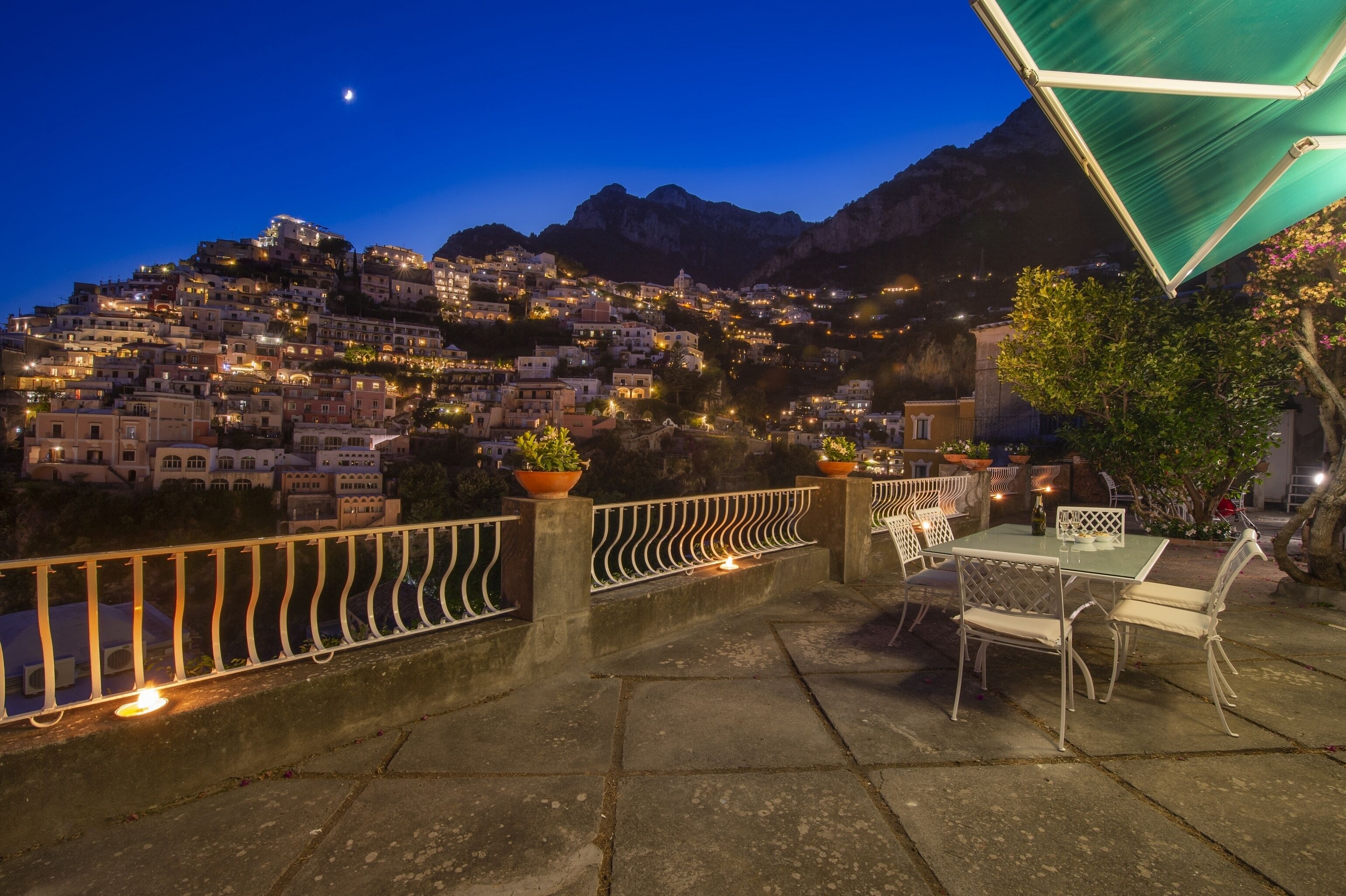 A terrace with a table and chairs, overlooking a town with buildings and mountains in the background.