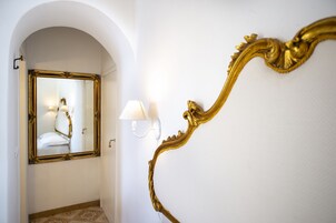 Un pasillo con un espejo dorado ornamentado y una lámpara fijada a la pared.