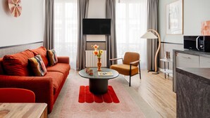 Una sala de estar moderna con un sofá rojo, una mesa de centro redonda y una zona de cocina con microondas.