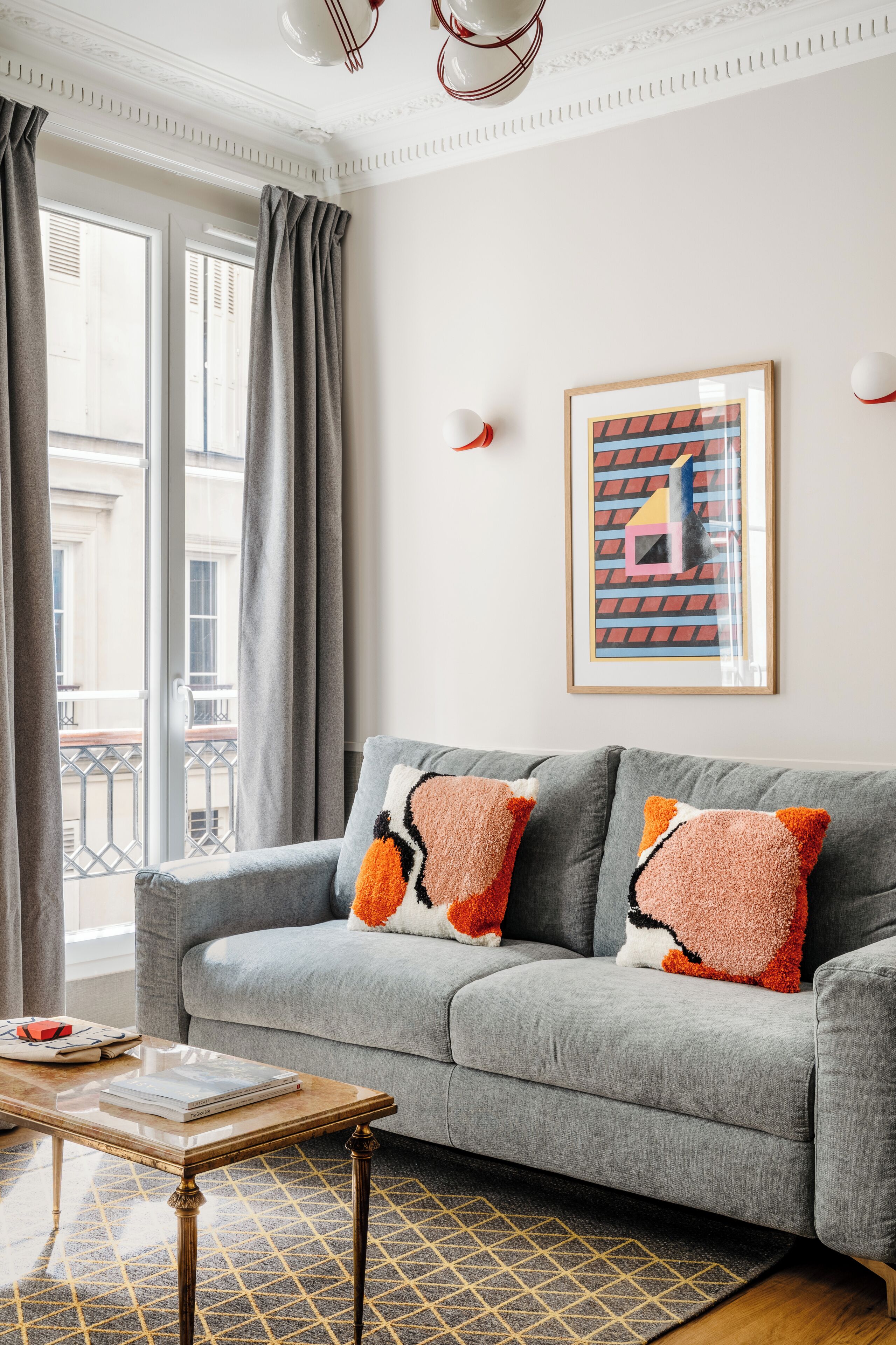 A modern living room with a grey sofa, patterned cushions, a framed abstract painting, and a patterned rug.