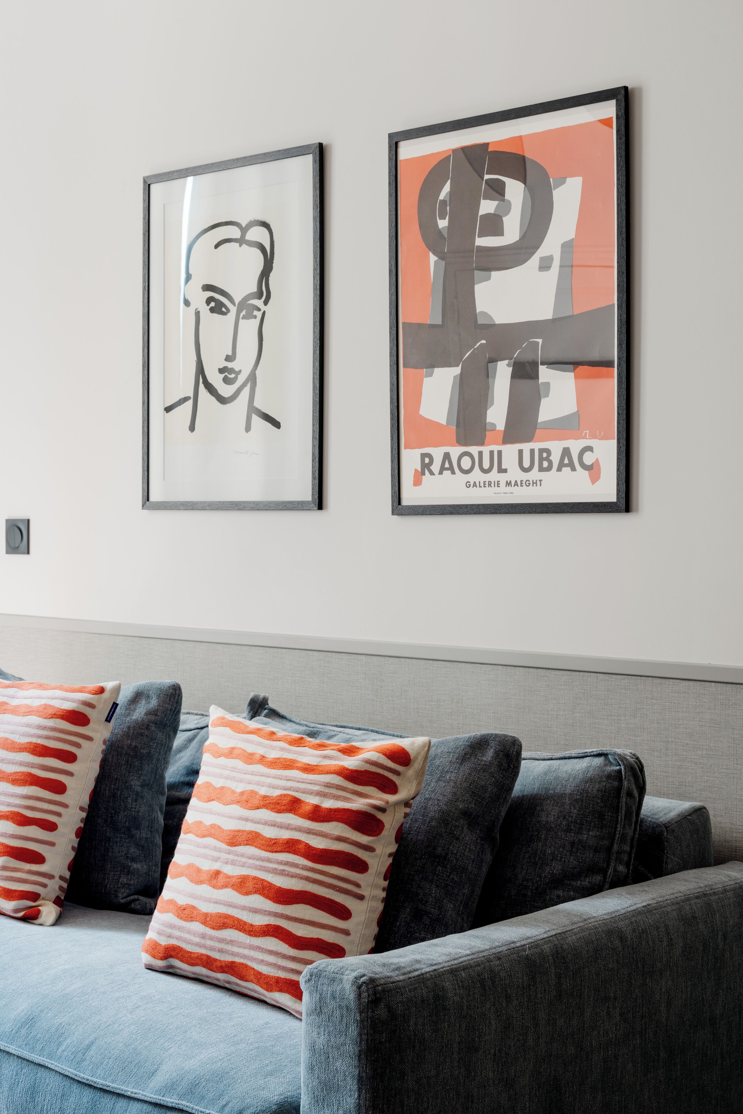 A living room with a grey sofa, two framed artworks, and patterned throw pillows.