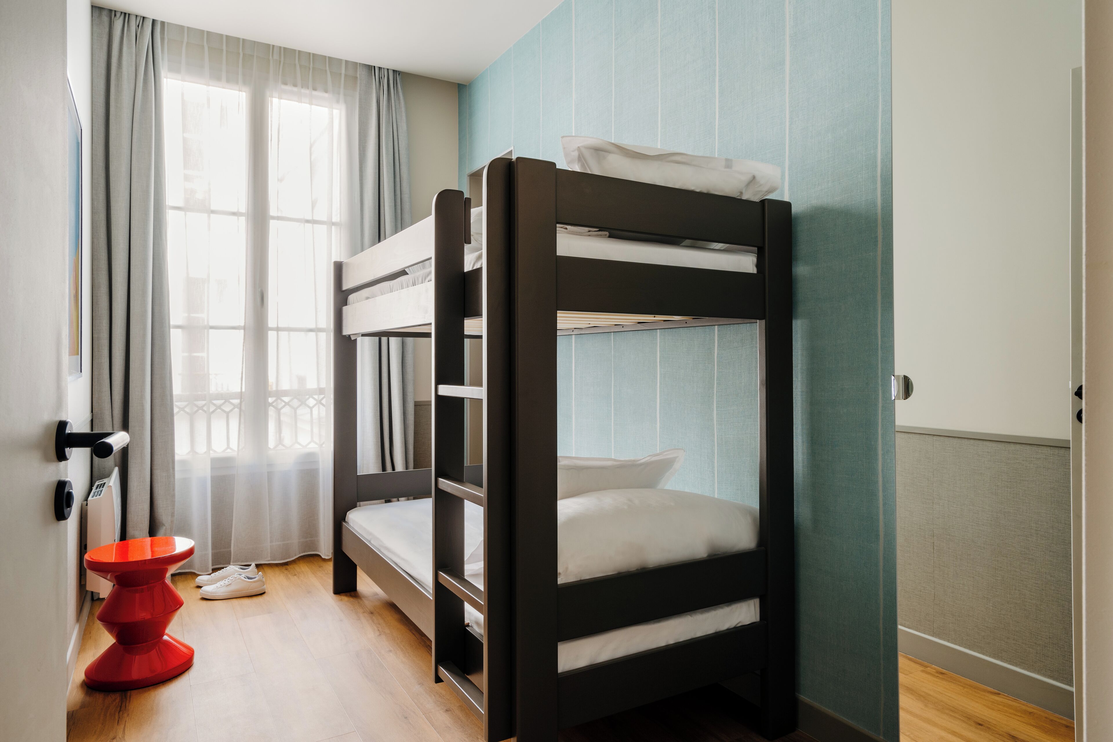 A bunk bed in a room with a window, a red chair, and a door.