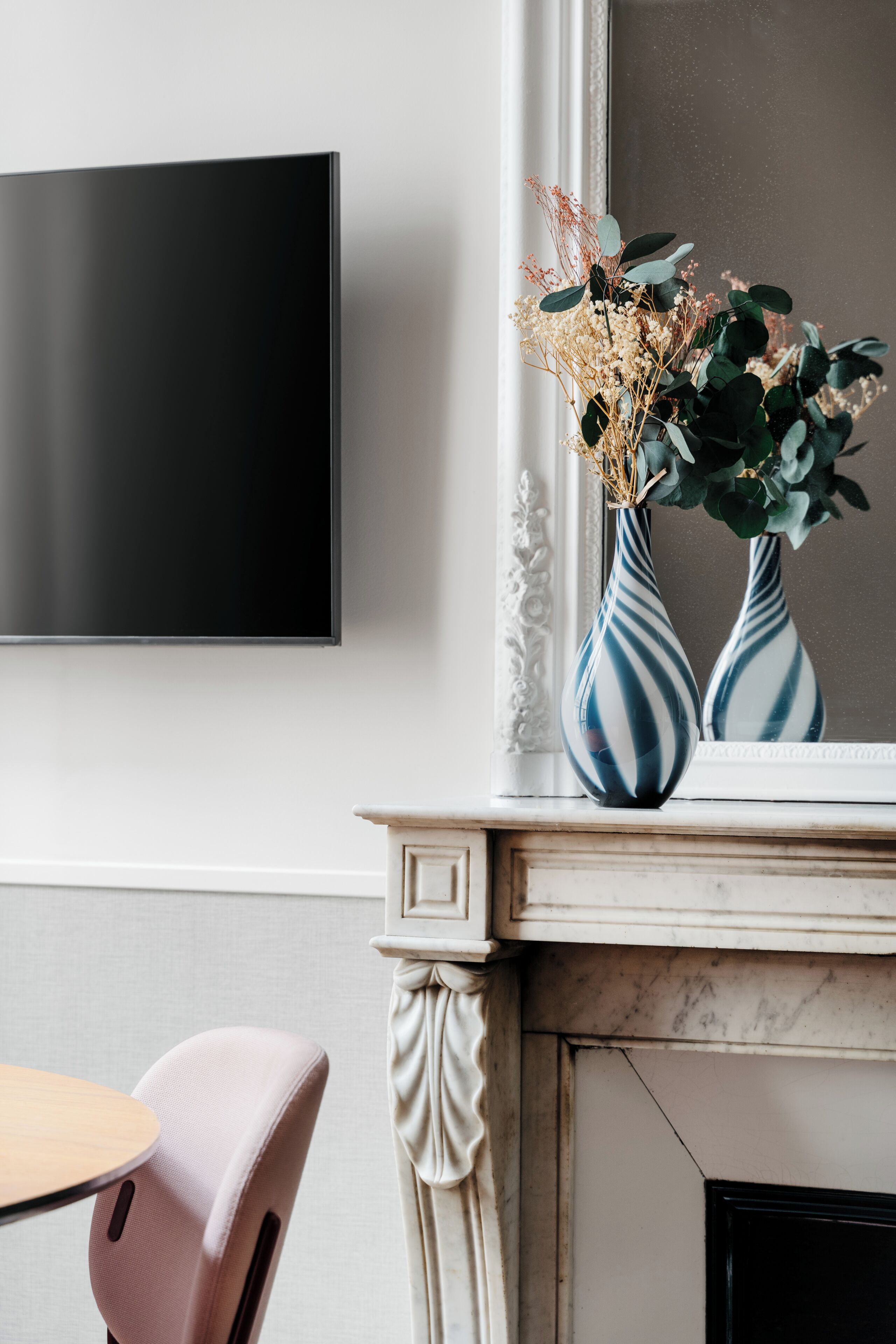 Una sala moderna con televisor de pantalla plana montado en la pared, repisa de chimenea con jarrones decorativos y una butaca rosa.
