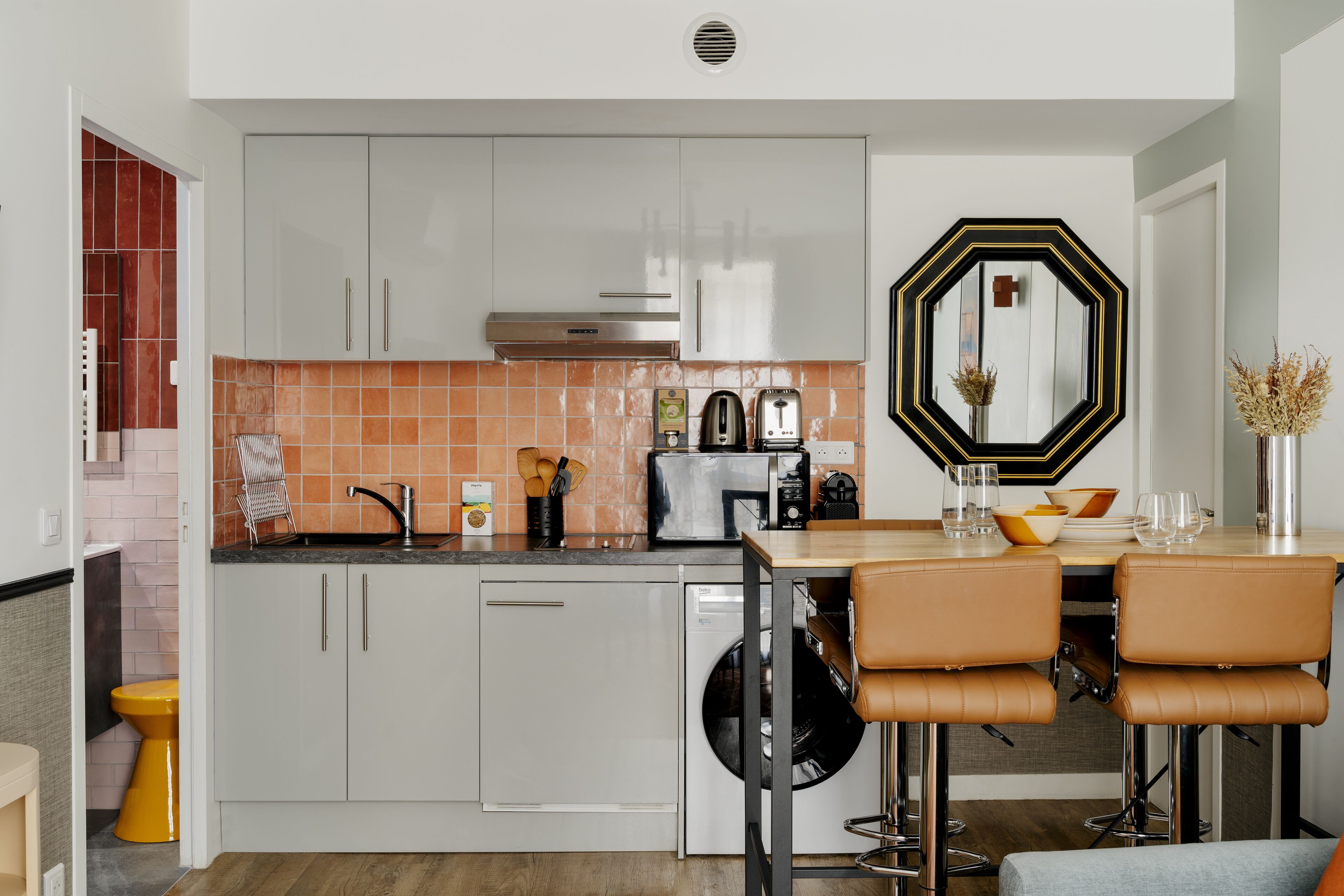 A modern kitchen with white cabinets, a black toaster, and a dining area with a wooden table and leather chairs.