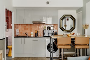 A modern kitchen with white cabinets, a built-in dishwasher, and a dining area with two brown leather chairs.