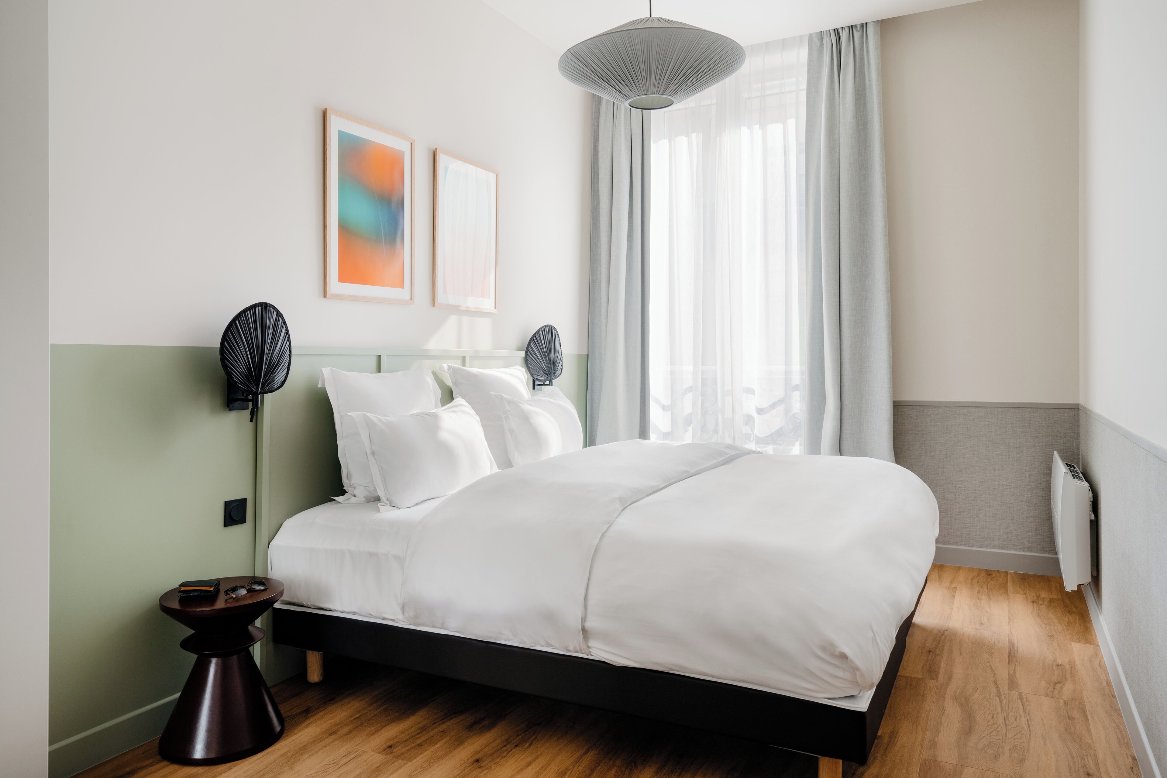 A modern hotel room with a large bed, bedside lamps, and a view of the outdoors through sheer curtains.