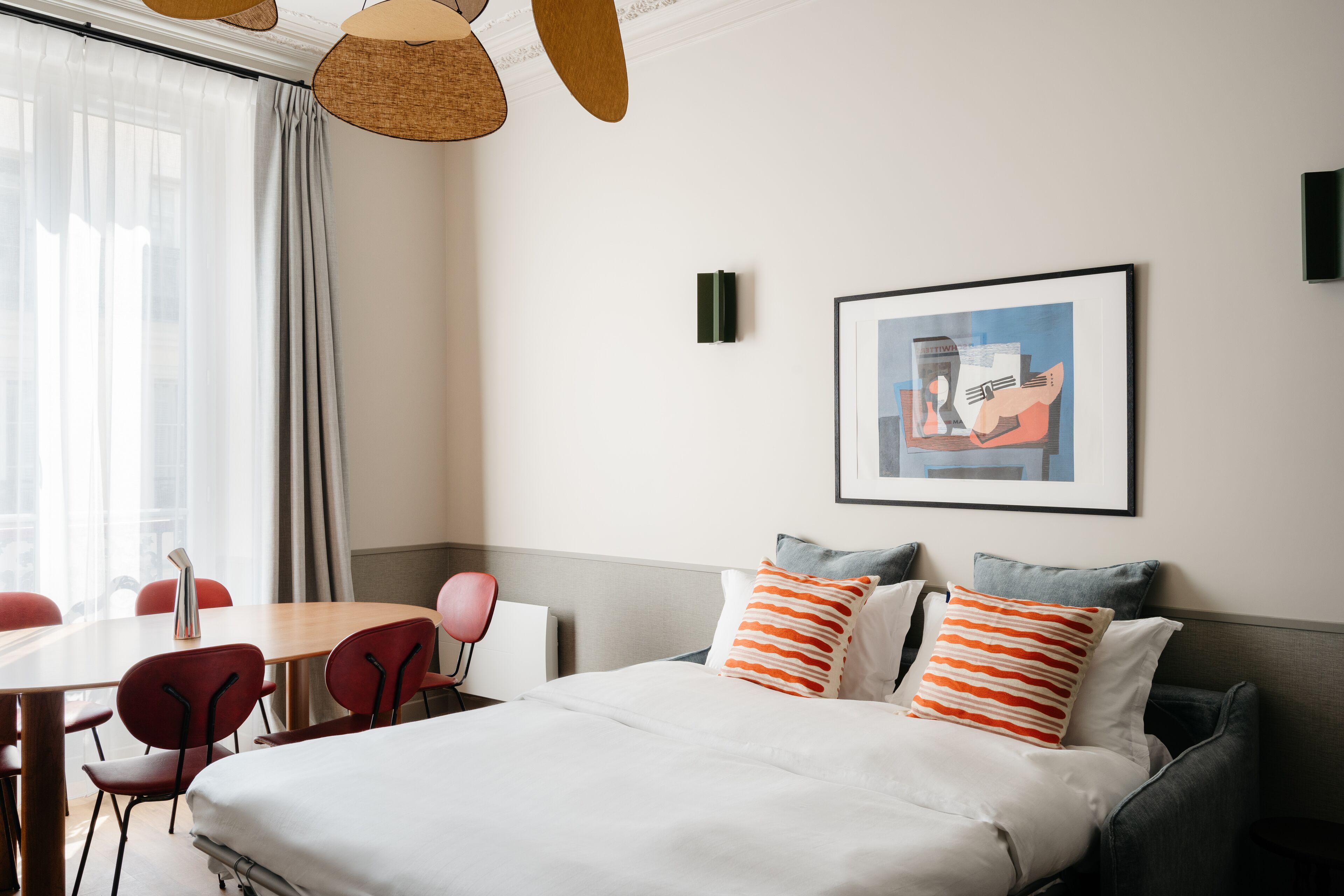 A hotel room with a bed, a dining table, chairs, and a framed artwork on the wall.