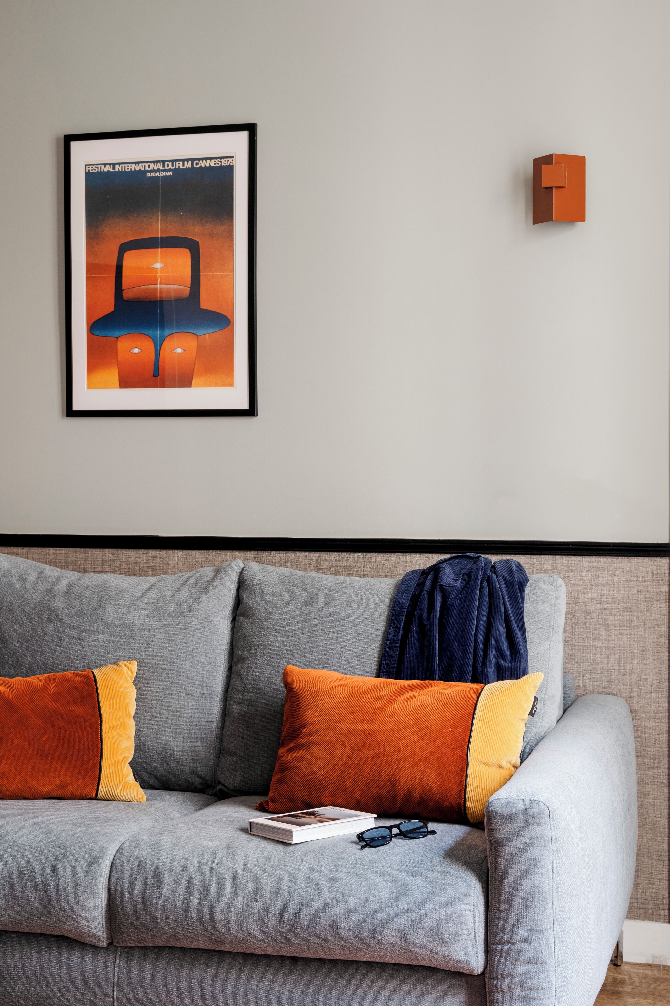 Un canapé gris avec des coussins orange et jaunes, un tableau encadré au mur et un petit objet orange accroché au mur.