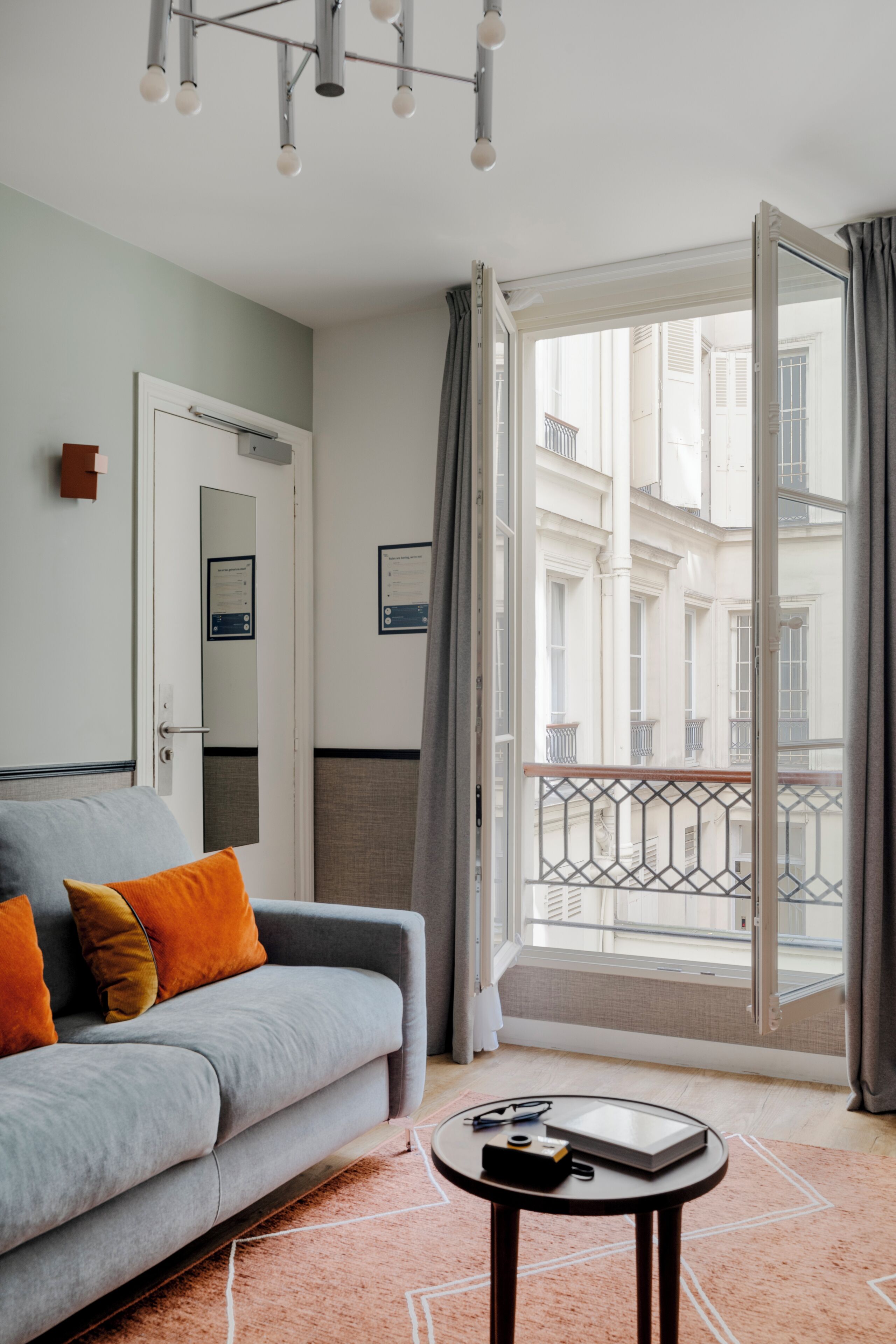 Una sala moderna con un sofá gris, una mesita redonda y vistas de un edificio a través de una puerta abierta.