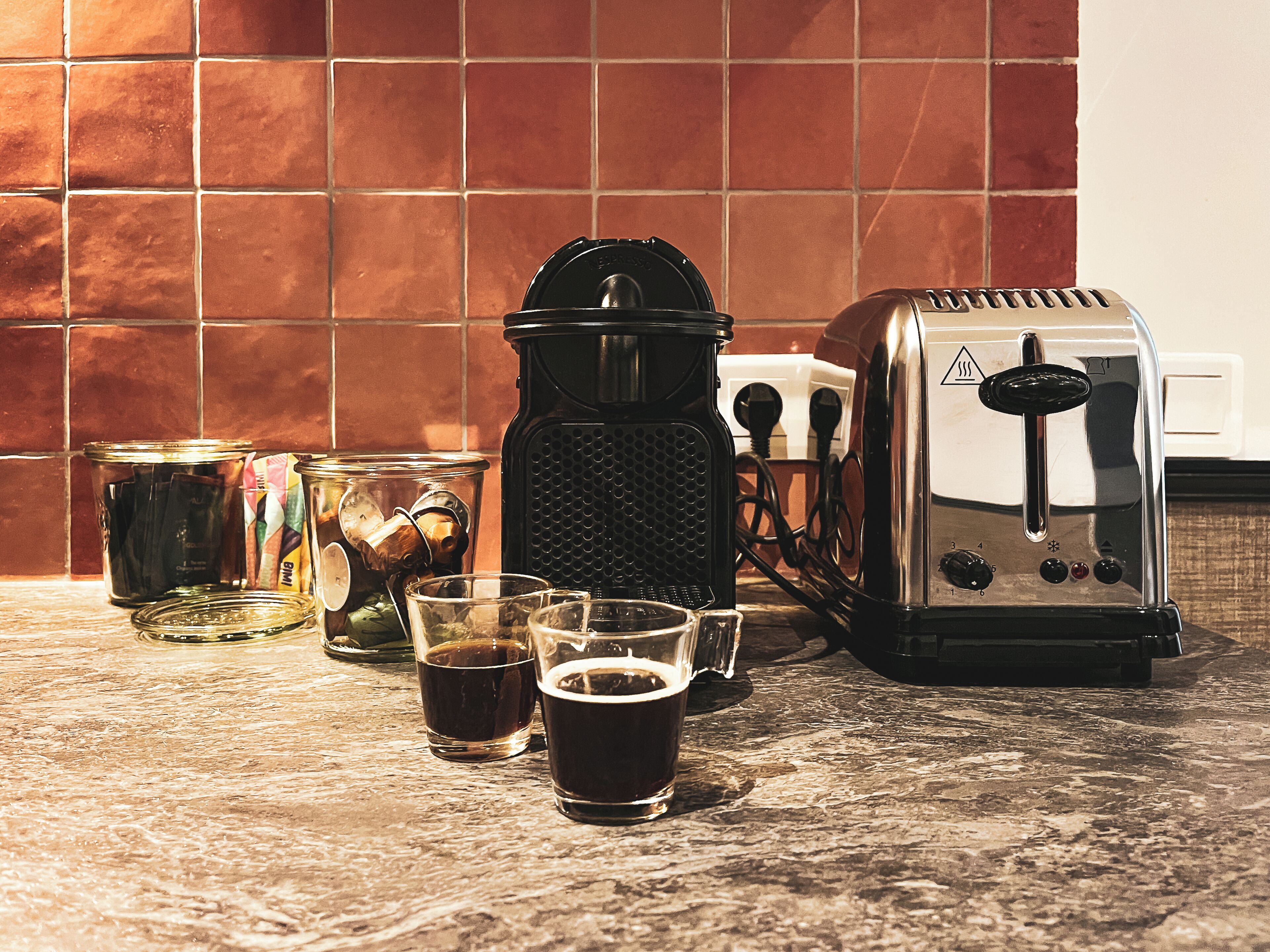 Un comptoir de cuisine avec une machine à café, un grille-pain et deux tasses de café.