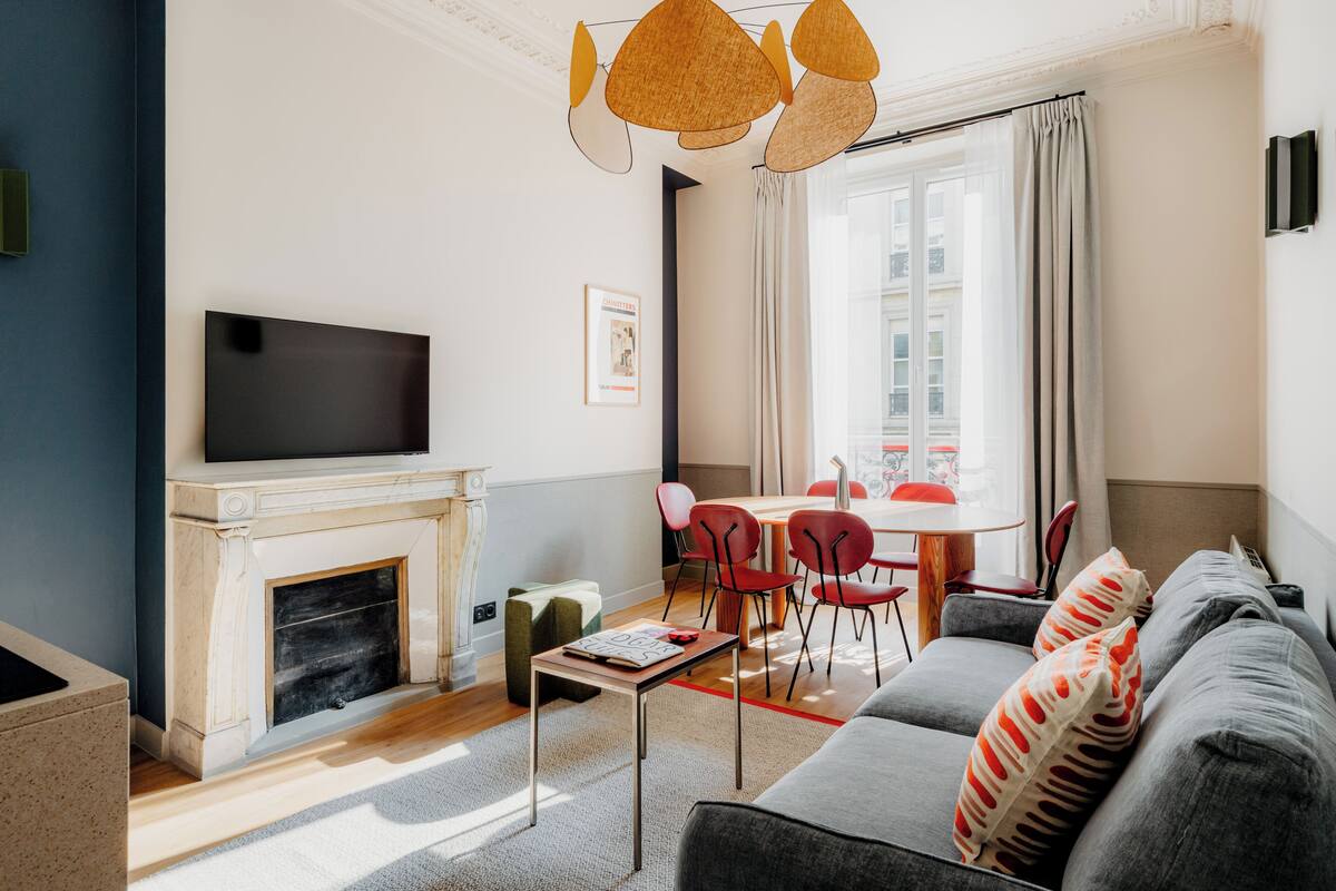 Una sala de estar moderna con chimenea, un televisor de pantalla plana, un comedor con sillas rojas y un ventanal con cortinas.