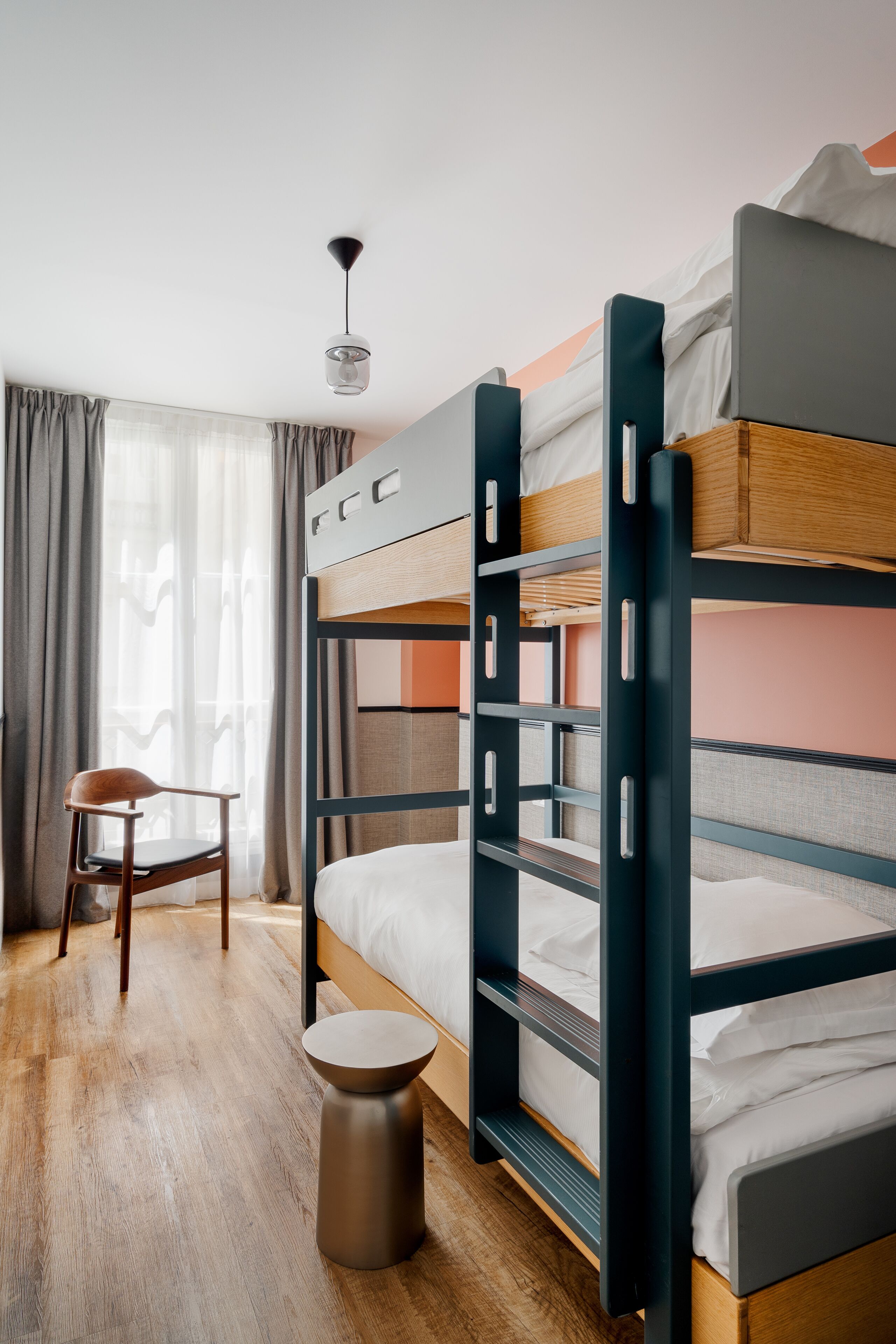 Habitación con literas, un escritorio, una silla, un taburete redondo y una lámpara colgante.