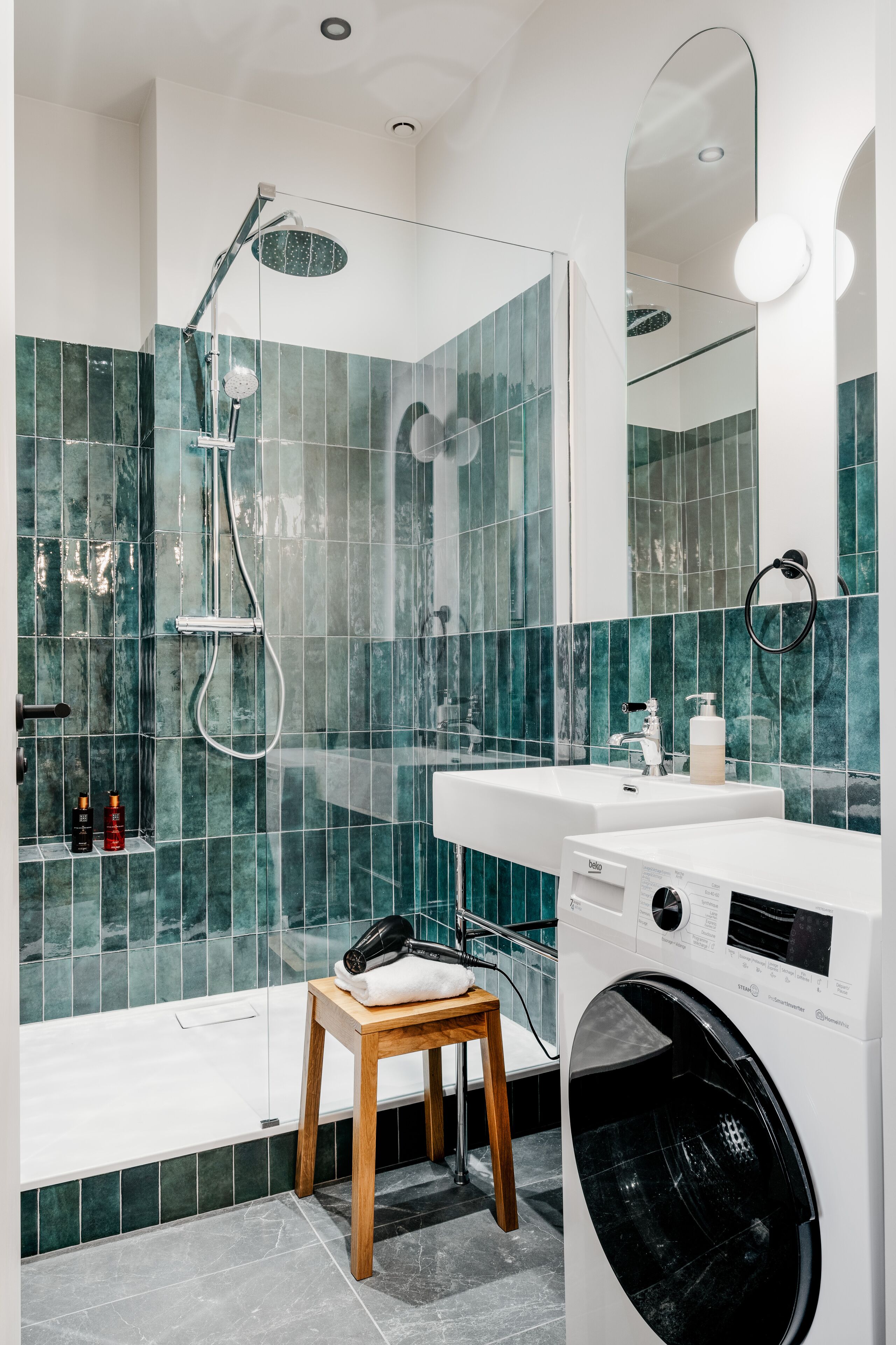A modern bathroom with a shower, a sink, a mirror, and a washing machine.