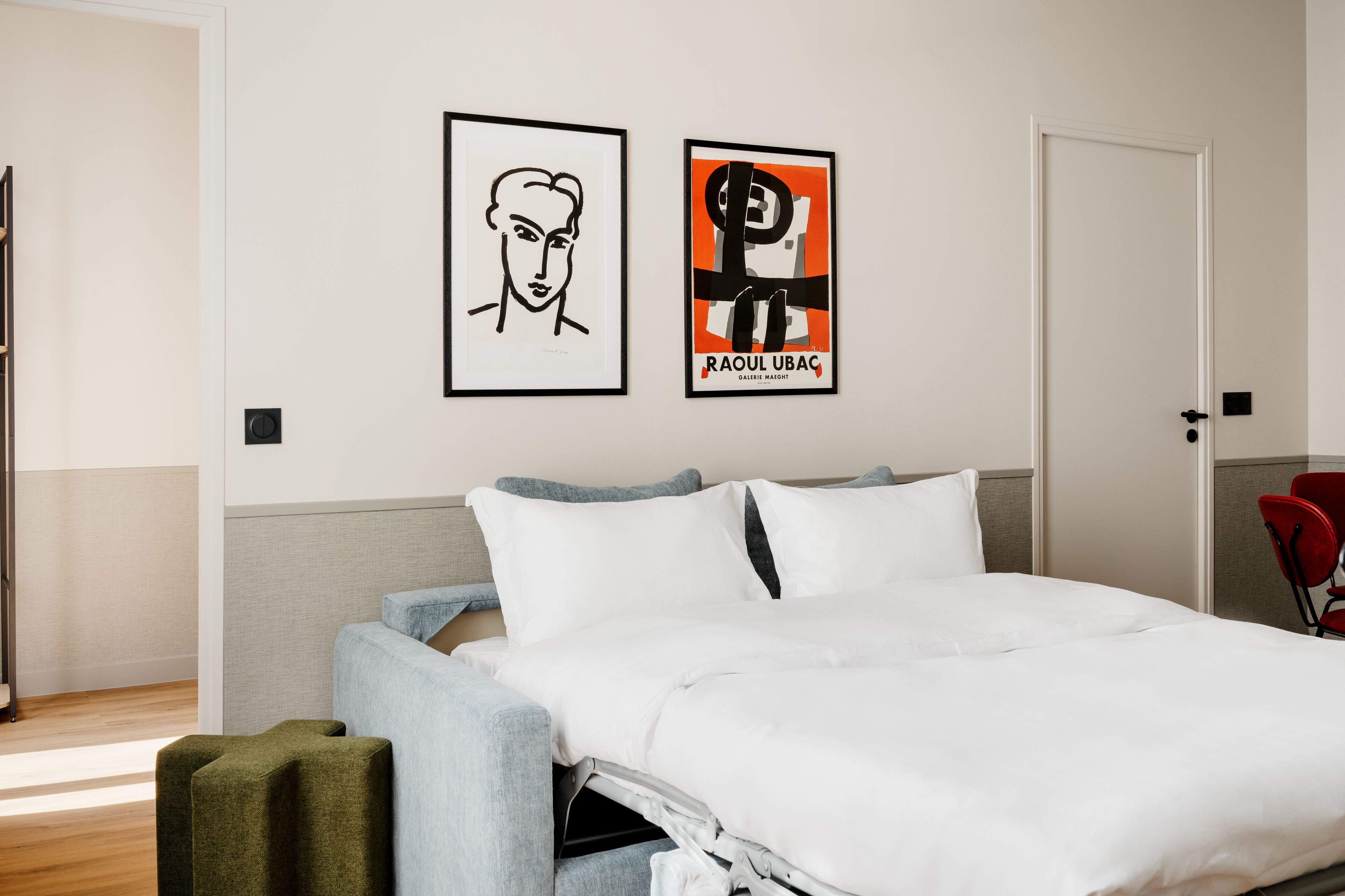 Ett hotellrum med en säng, en stol och två inramade konstverk på väggen.