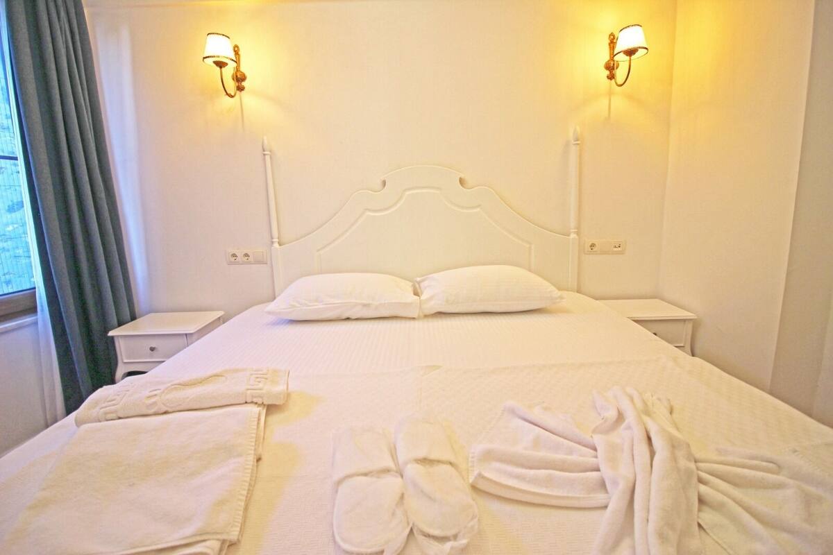 A neatly made bed with white linens, two bedside lamps, and a window with curtains.