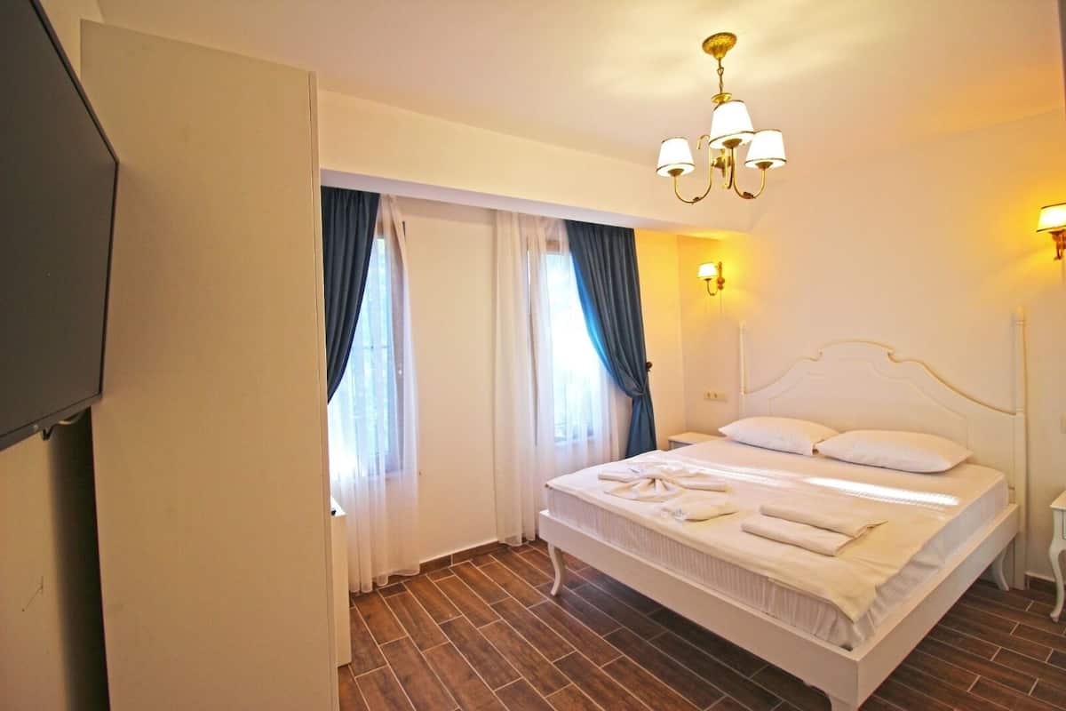 A hotel room with a large bed, two bedside lamps, a chandelier, and a TV mounted on the wall.