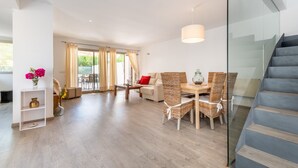 A modern living room with a dining area, a staircase, and a glass railing. - Holiday Home “Aloe” with Garden, Terraces & Wi-Fi (Son Serra de Marina)