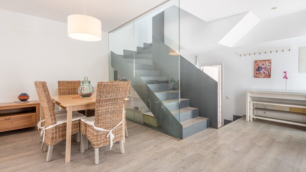 A modern interior with a dining area, wicker chairs, a glass staircase, and a minimalist design. - Holiday Home “Aloe” with Garden, Terraces & Wi-Fi (Son Serra de Marina)