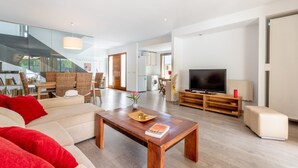 A modern living room with a sofa, coffee table, TV, and a dining area with chairs and a table. - Holiday Home “Aloe” with Garden, Terraces & Wi-Fi (Son Serra de Marina)