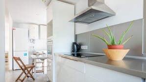 A modern kitchen with white cabinetry, a stainless steel range hood, a wooden chair, and a potted plant on the counter. - Holiday Home “Aloe” with Garden, Terraces & Wi-Fi (Son Serra de Marina)