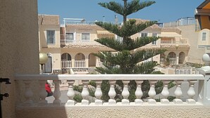 A balcony with a potted tree, a tiled floor, and a view of buildings in the background.