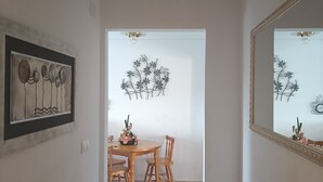 A hallway leading to a dining area with a wooden table and chairs, a framed artwork on the wall, and a mirror reflecting the room.