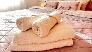 A neatly made bed with a quilted cover and rolled towels stacked on top.