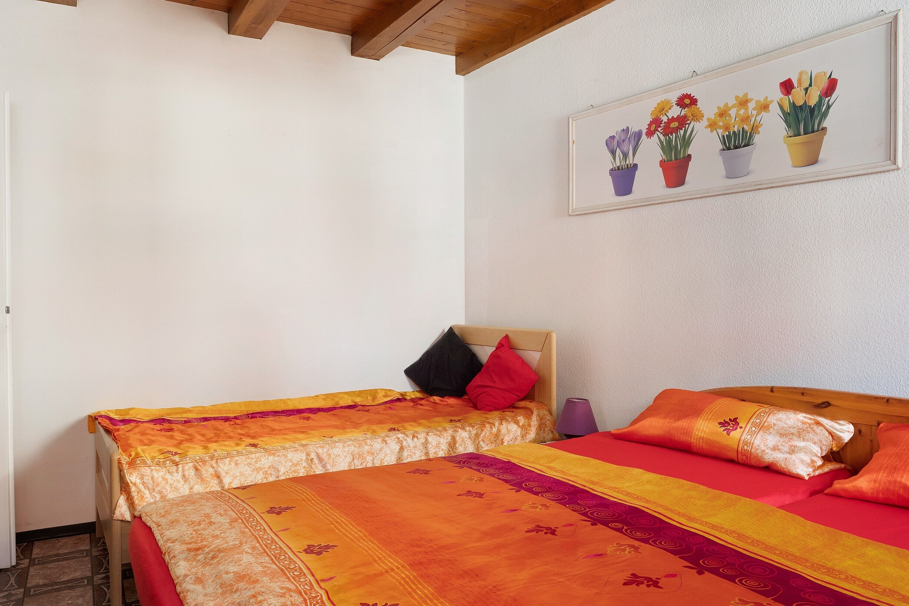 A room with two beds, a wooden ceiling, and a wall-mounted picture of potted flowers.