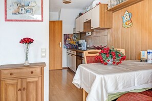 A room with a wooden cabinet, a dining table with a white tablecloth, and a vase of red flowers. - Central Apartment "Reichenaublick" on Lake Constance with Lake and Mountain Views (Allensbach)