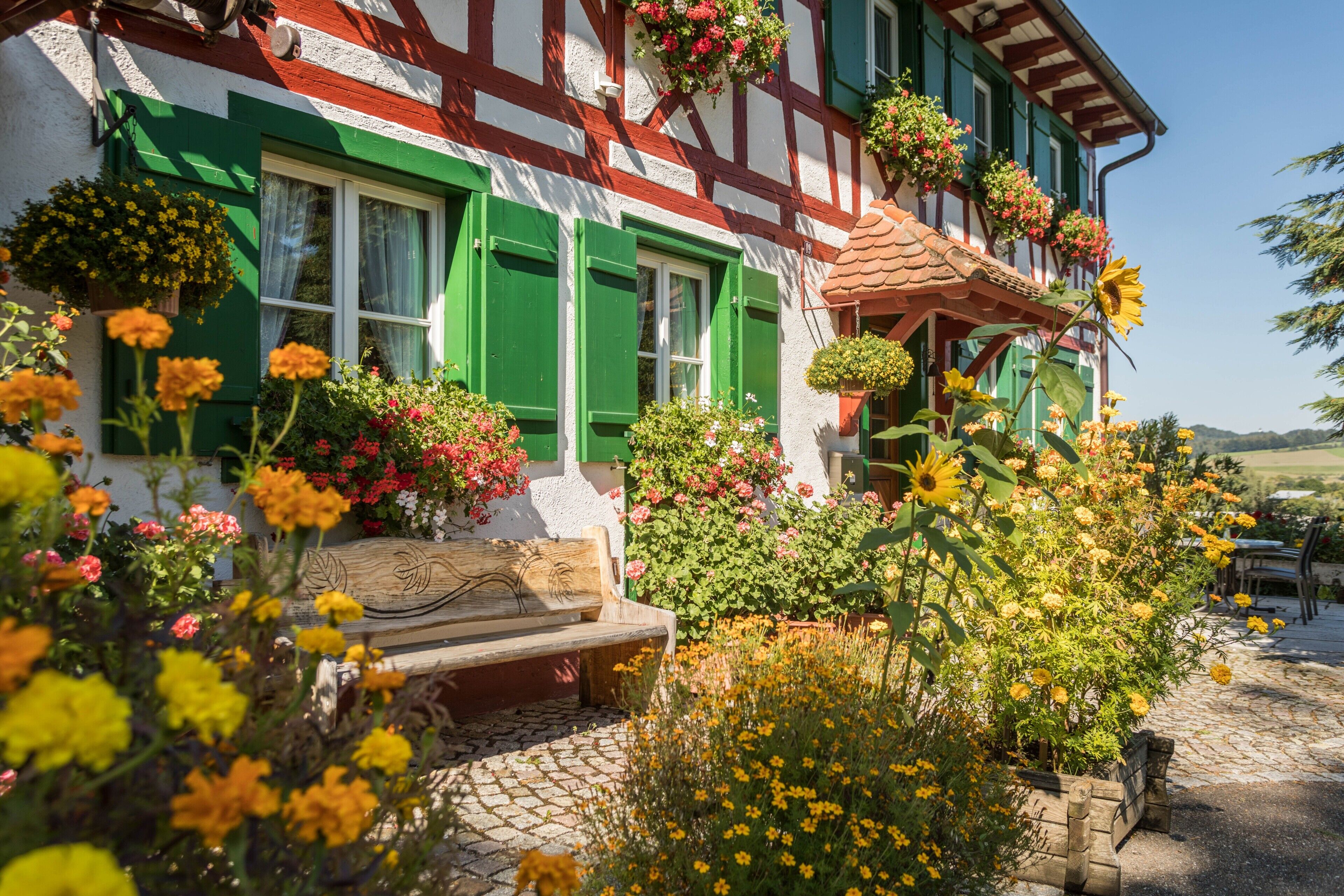 Ein traditionelles Fachwerkhäuschen mit einem Steinweg, einer hölzernen Bank und Blumenkästen an den Fensterbänken.