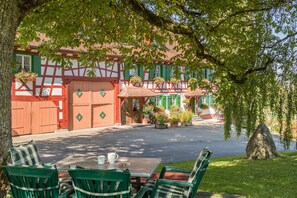 Un bâtiment traditionnel à colombages, avec une porte rouge, des volets verts et des plantes en pot.