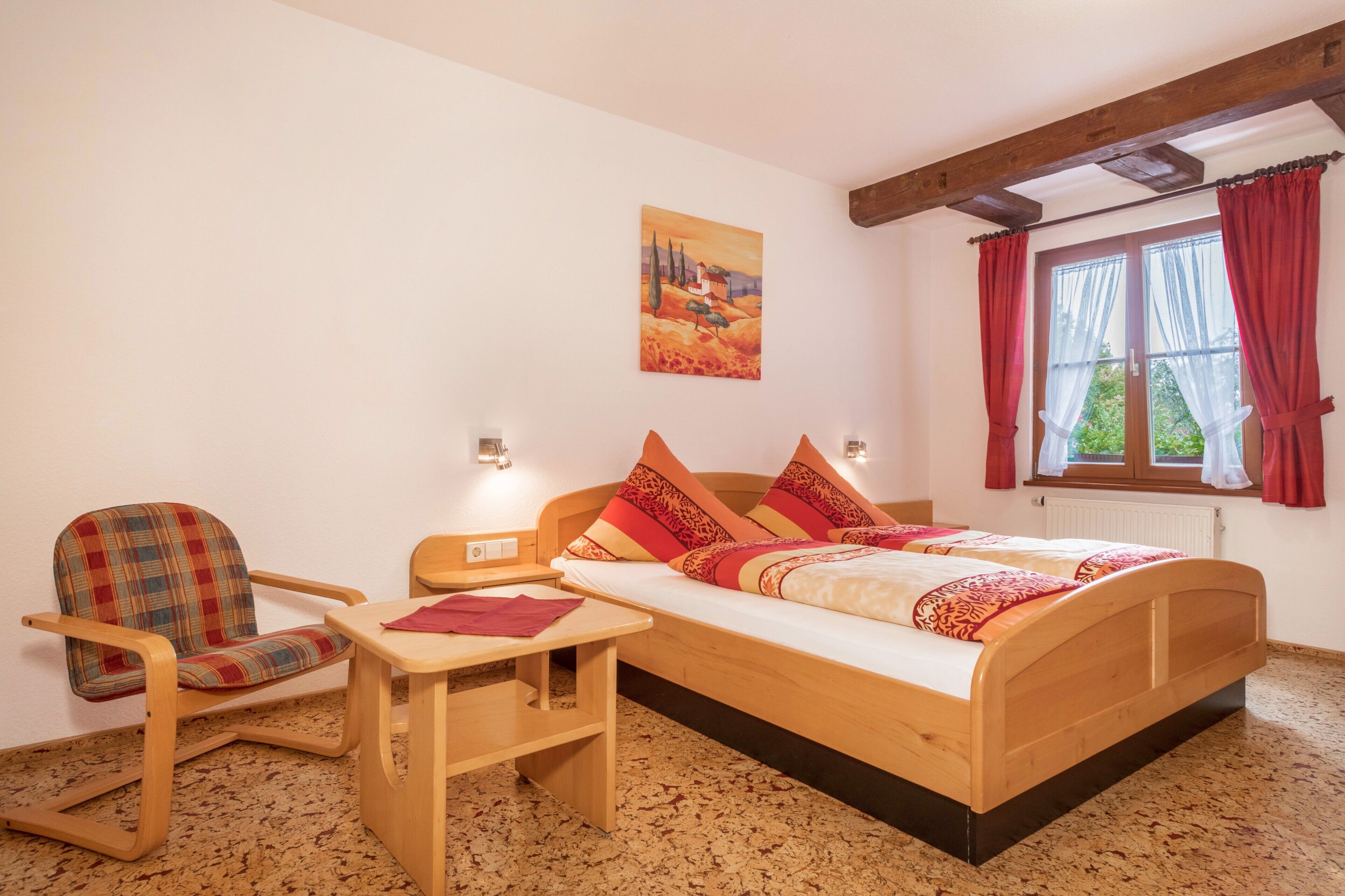 Une pièce avec un lit en bois, une chaise, une petite table et un tableau accroché au mur.