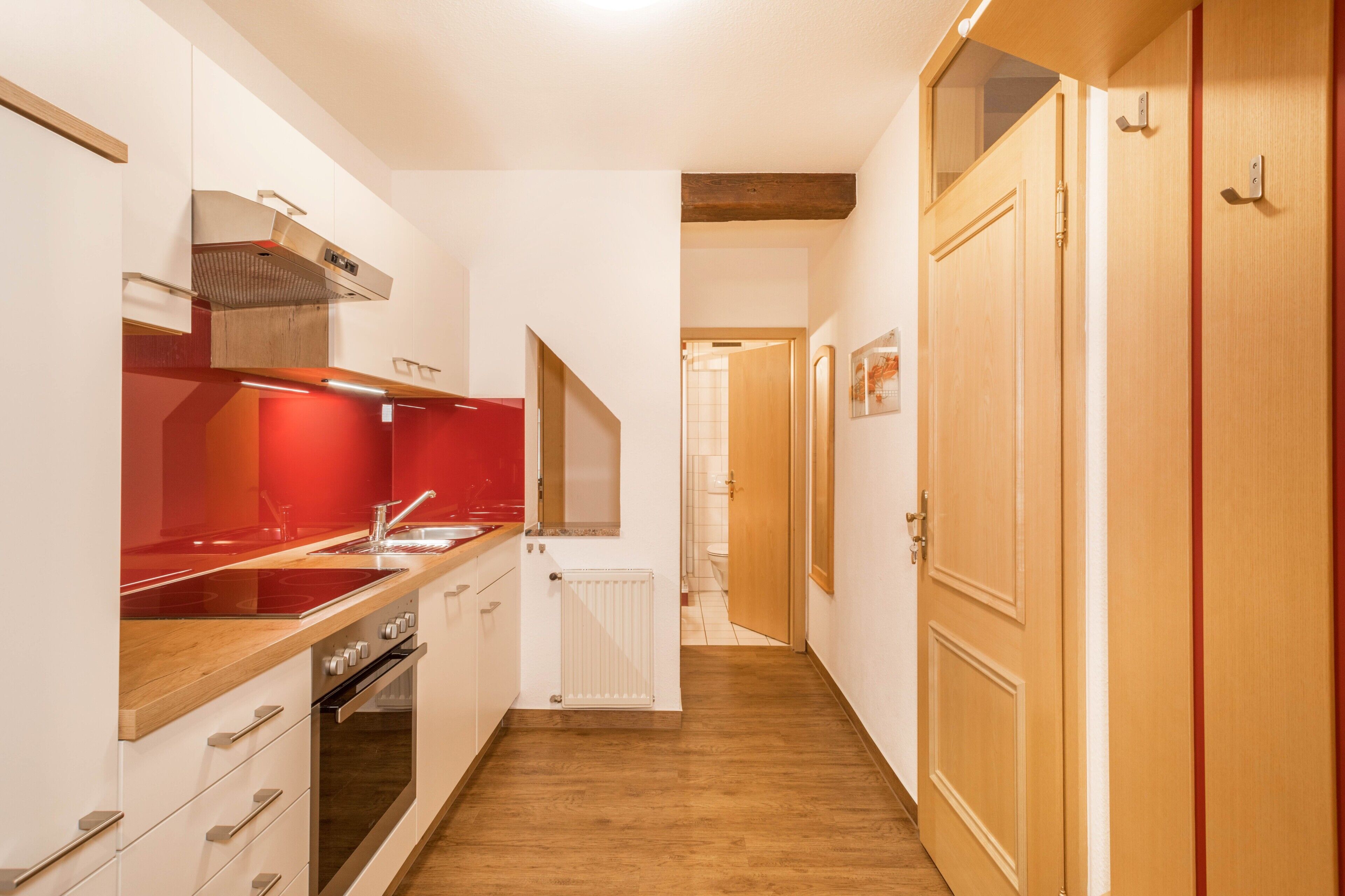 A narrow hallway leading to a kitchen with a red countertop, a built-in oven, and a radiator.
