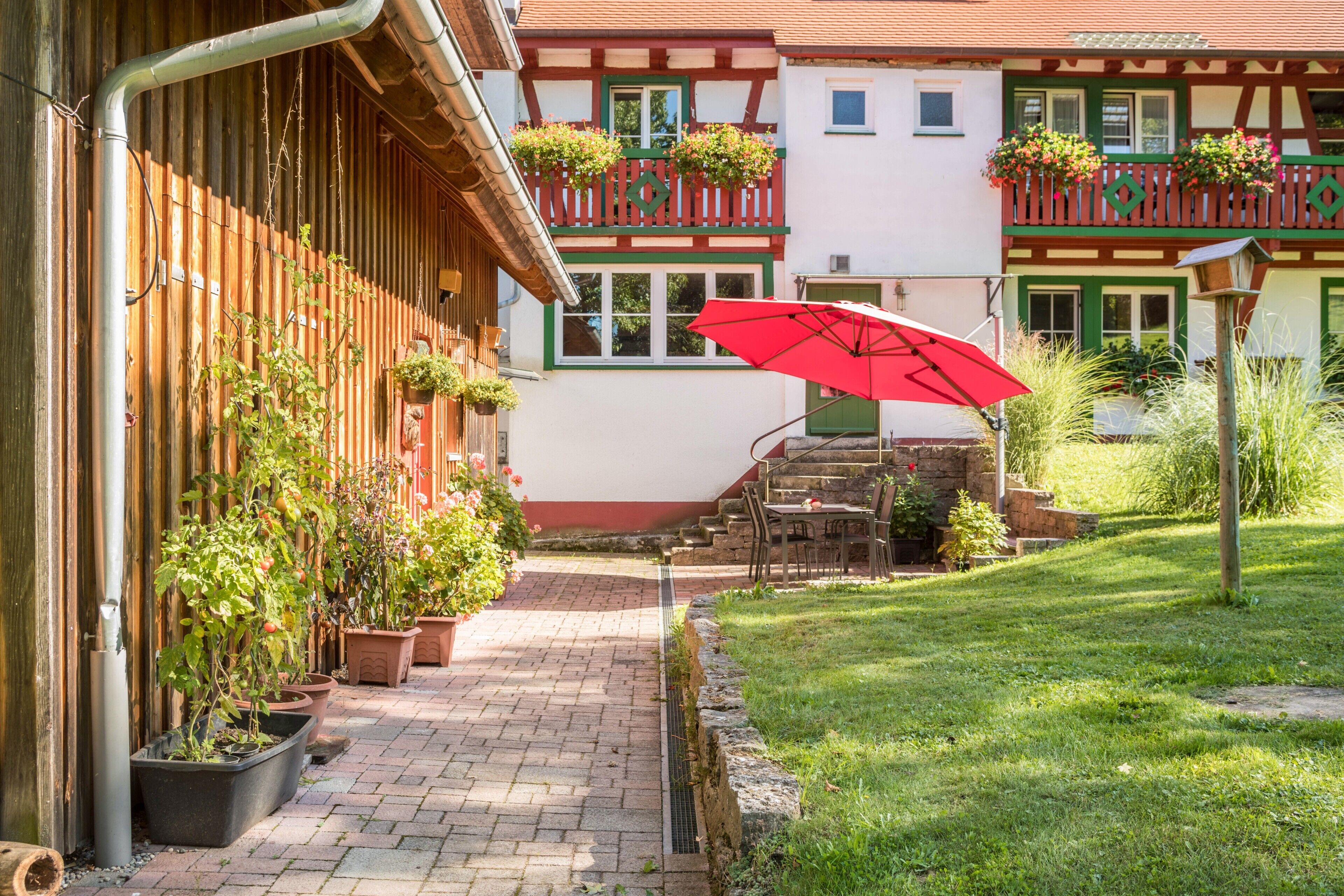 Ein Innenhof mit rotem Sonnenschirm, Blumentöpfen und einem Gebäude mit Balkon.